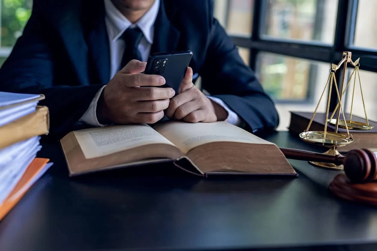 Business professional sitting at a desk wearing a suit and holding a smartphone reviewing legal precedents while researching contract playbook data